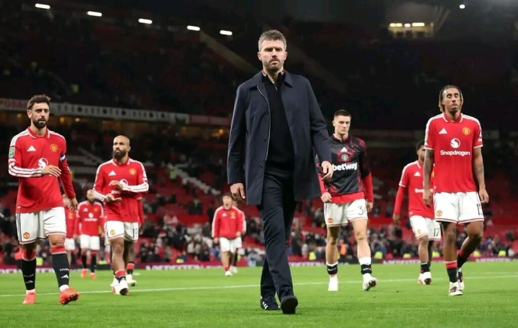 Michael Carrick caminha cabisbaixo à frente dos jogadores do Manchester United em Old Trafford, sinal de pressão sobre o comando técnico na Premier League 2026/27